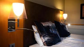 Yölamppu ja tyynyjen yksityiskohtia Standard-huoneessa, Clarion Collection Hotel Kompaniet -hotellissa, Nyköpingissä