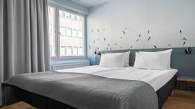 Moderni kahden hengen Standard-huone parivuoteella, harmaalla sängynpäädyllä, harmailla verhoilla sekä seinällä olevalla kuvioinnilla, Quality Hotel Grand Kristianstad -hotellissa